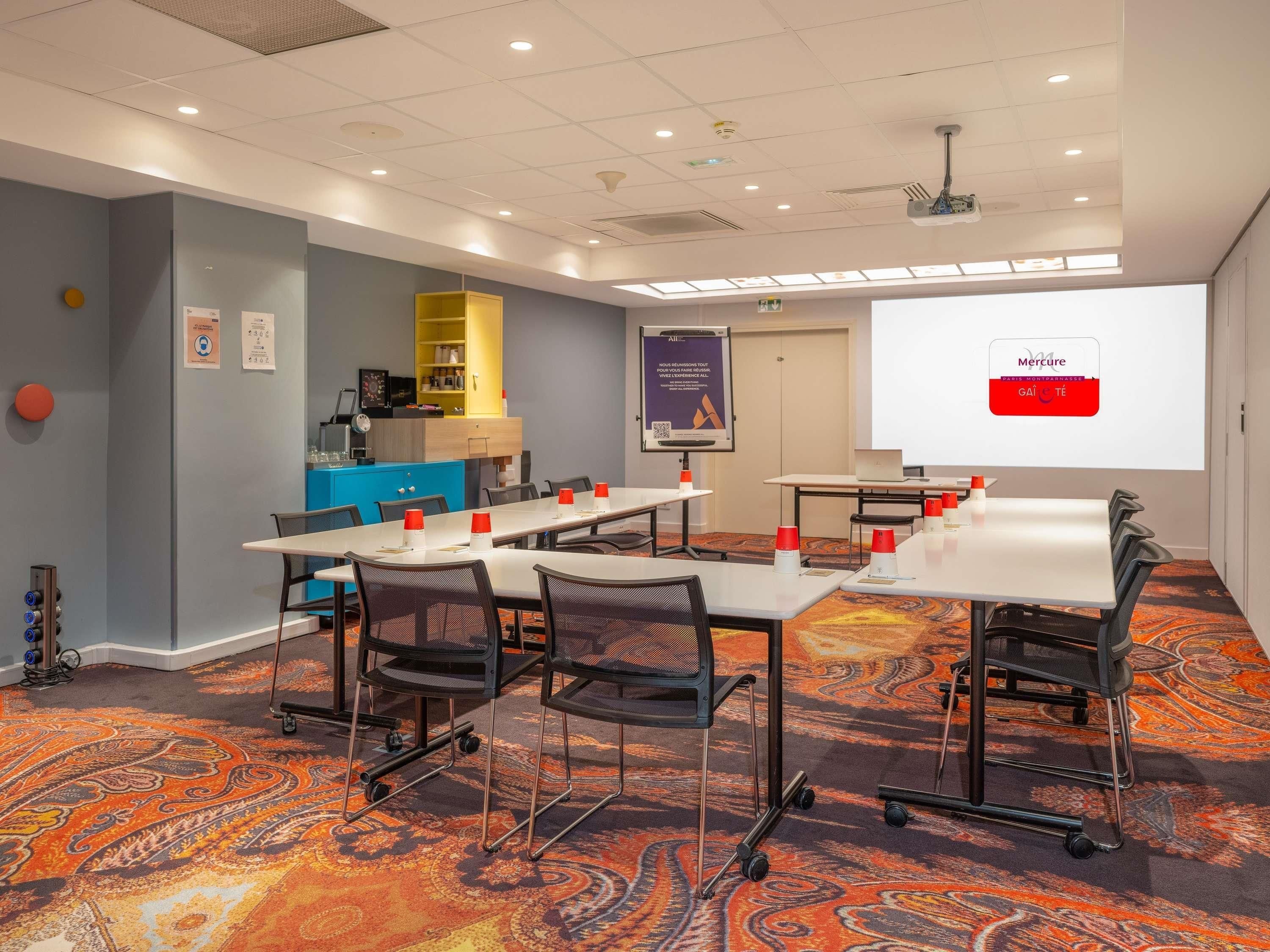 A conference room with tables, chairs, a projector screen, and a presentation on the wall.