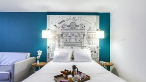 A hotel room with a bed, a tray with breakfast items, a white pillow, a lamp, and a wall with Paris-themed artwork.