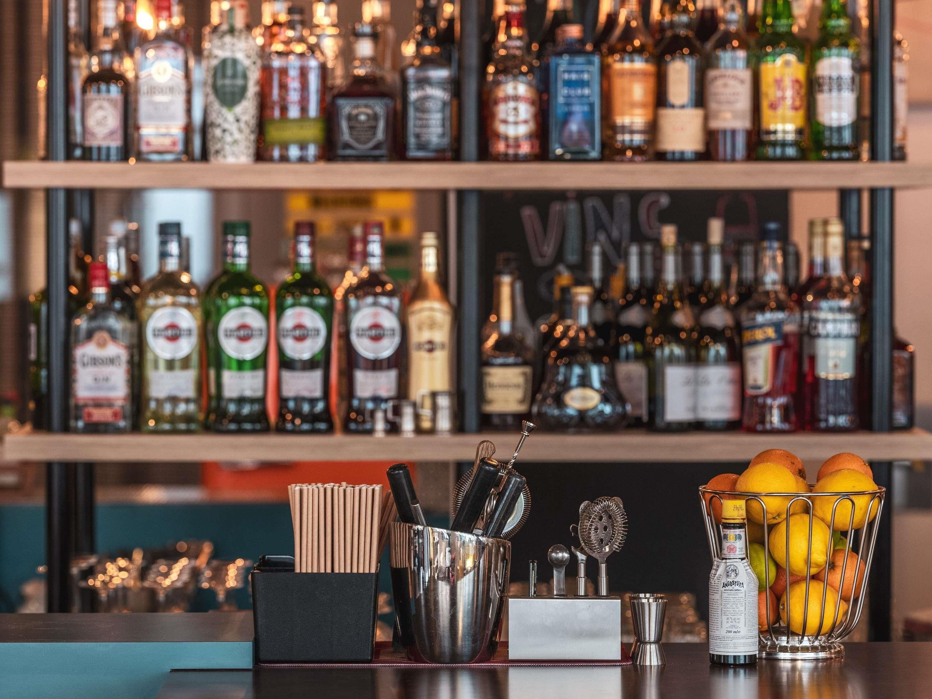 A bar area with a variety of liquor bottles, a metal bar tool set, and a fruit basket.