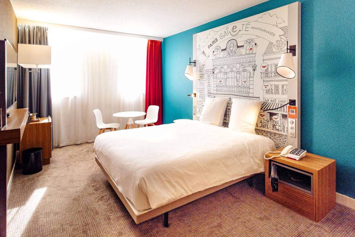 Hotelkamer met een bed, bureau, stoel, klein tafeltje, lamp en een muur met een kaart.