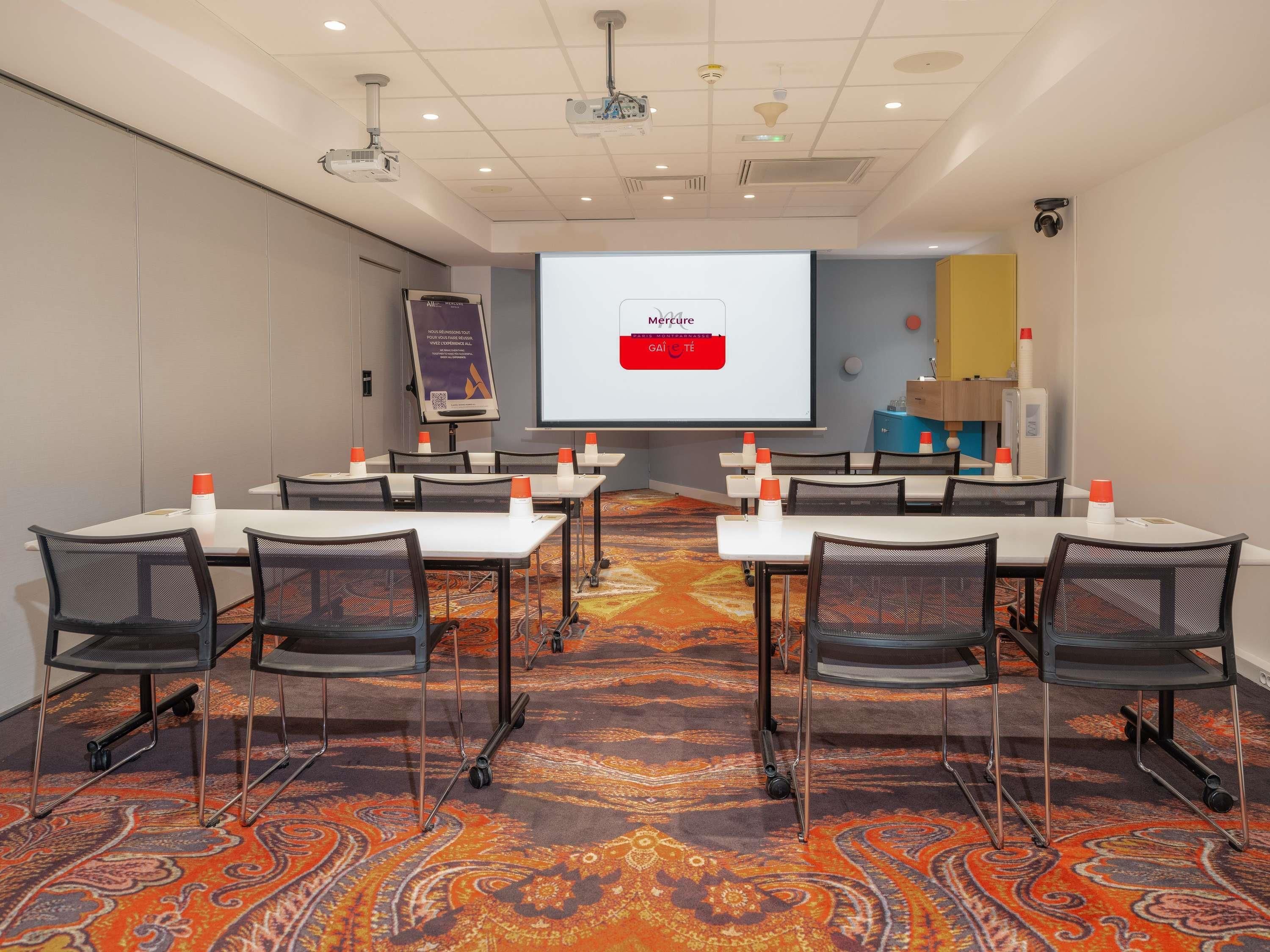 A conference room with tables, chairs, a projector screen, and a presentation screen.
