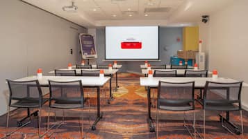 A conference room with tables, chairs, a projector screen, and a presentation screen.