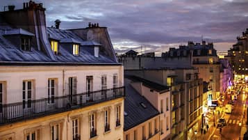 A cityscape at dusk with buildings featuring balconies and a street with pedestrians.
