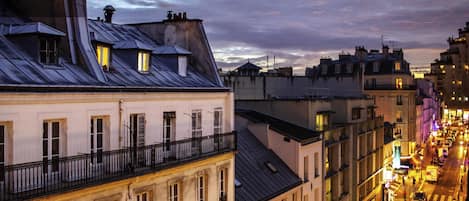 A cityscape at dusk with buildings featuring balconies and a street with pedestrians.