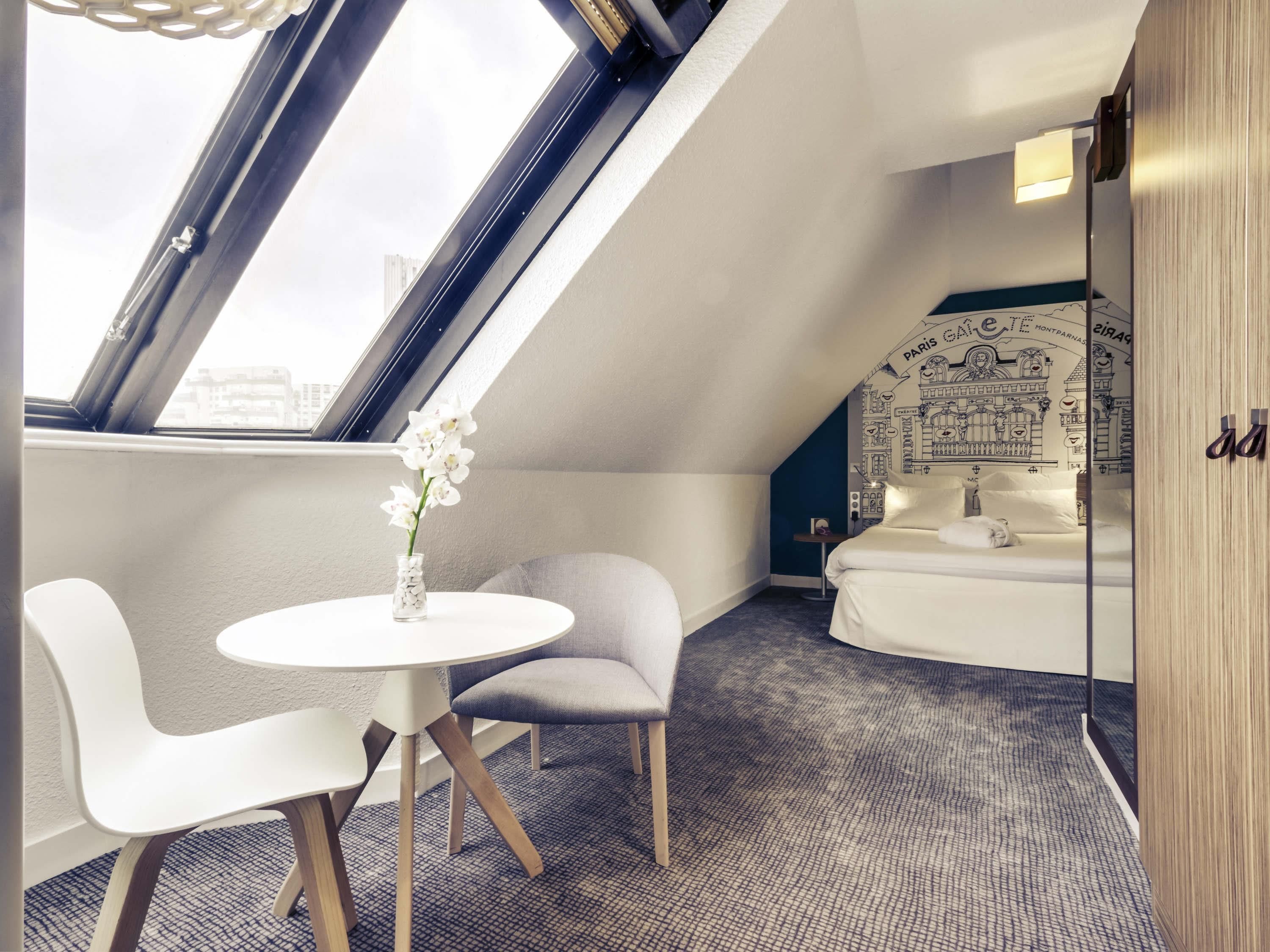 A modern room with a skylight, a round table, two chairs, a small round table, a bed with a city-themed headboard, and a mirror.