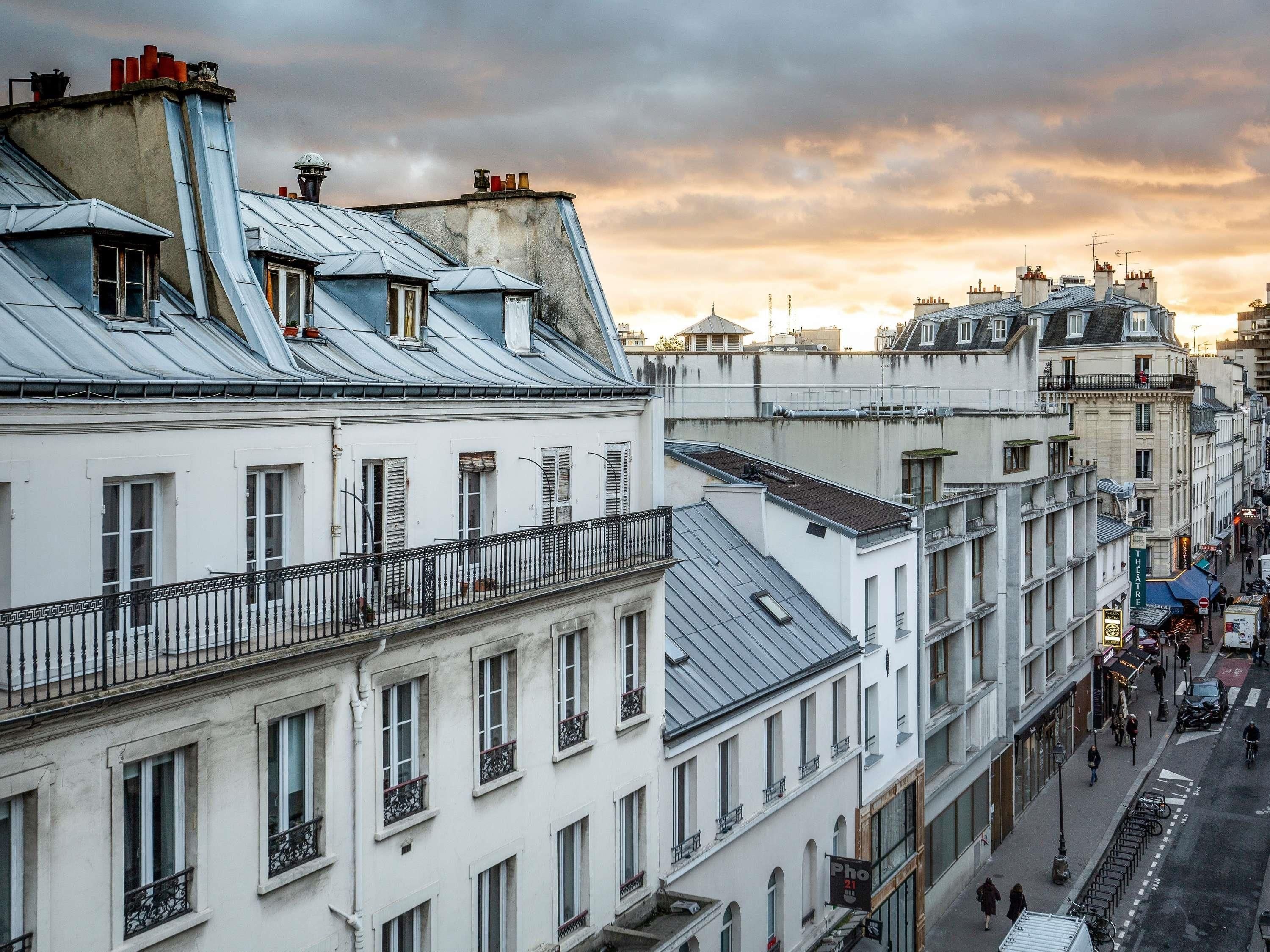 Une rangée de bâtiments blancs dotés de balcons, une rue animée de piétons et un ciel dégagé.