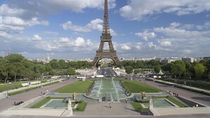 The Eiffel Tower in Paris with a clear sky and surrounding greenery.