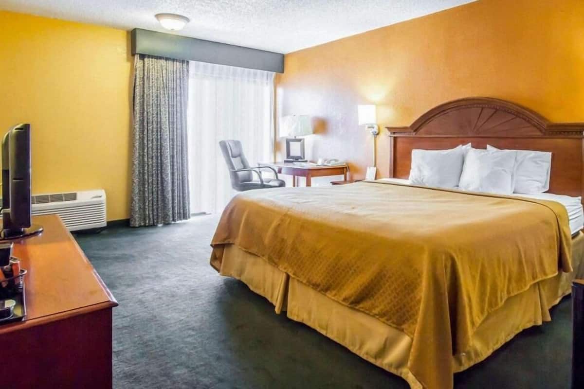 Hotellihuone, jossa on sänky, työpöytä tietokoneella, tuoli, televisio ja ilmastointilaite.