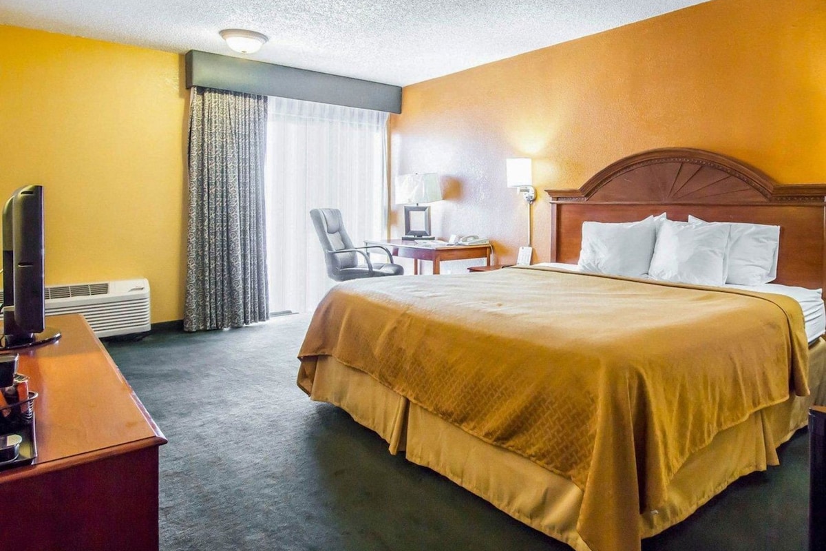 Een hotelkamer met een bed, bureau, stoel, televisie en een raam met gordijnen.
