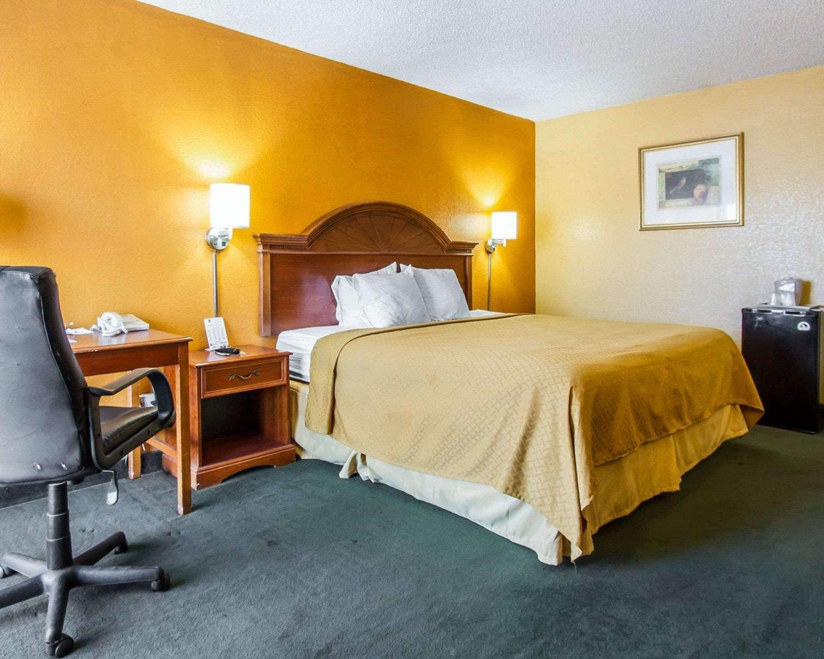 Une chambre d’hôtel comprenant un lit, une table de chevet, une lampe, un bureau, une chaise et un petit réfrigérateur.