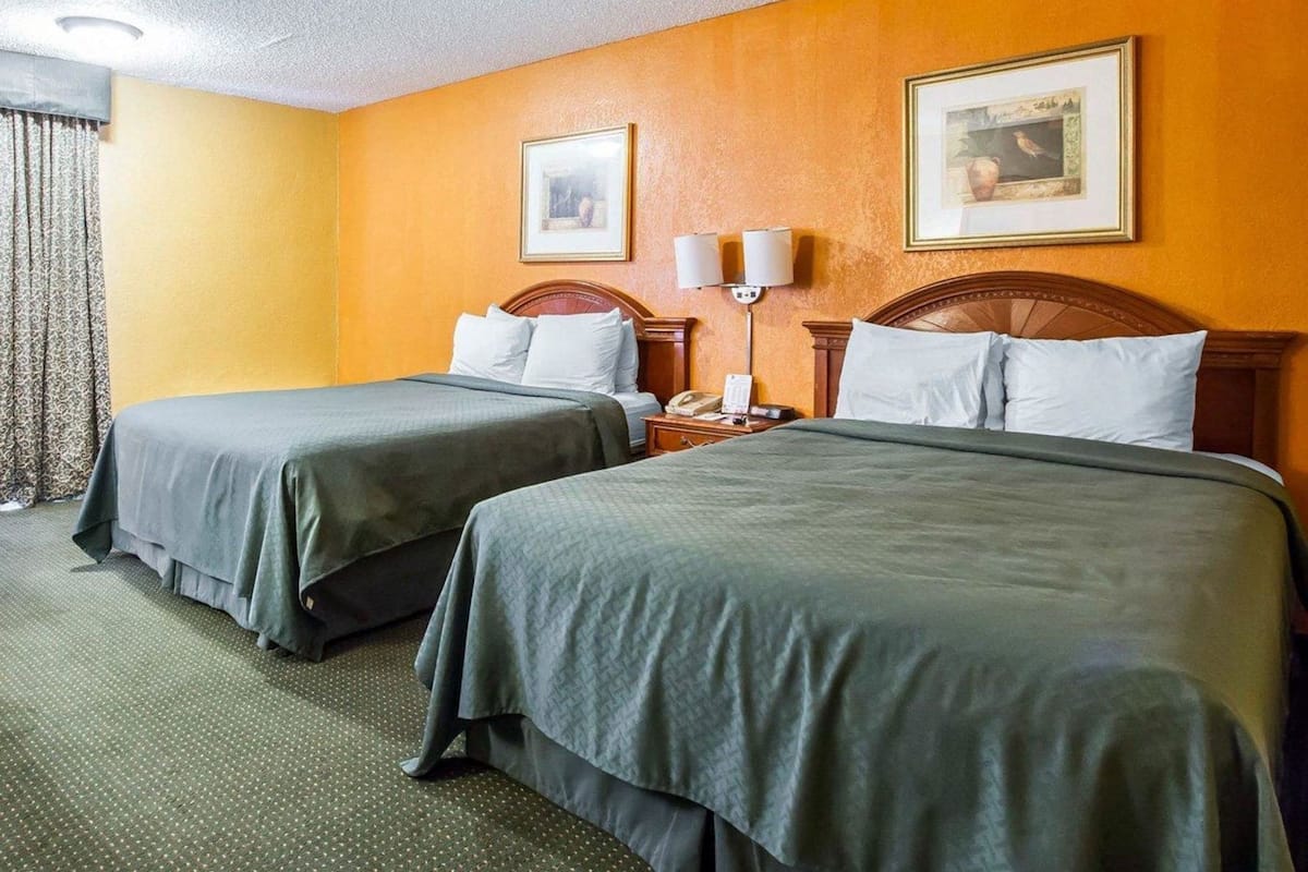 Hotellihuone, jossa on kaksi sänkyä, yöpöytä, lamppu ja seinällä oleva kehystetty kuva.