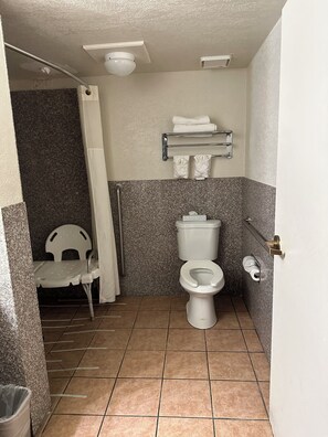 A small bathroom with a toilet, a shower chair, and a towel rack.