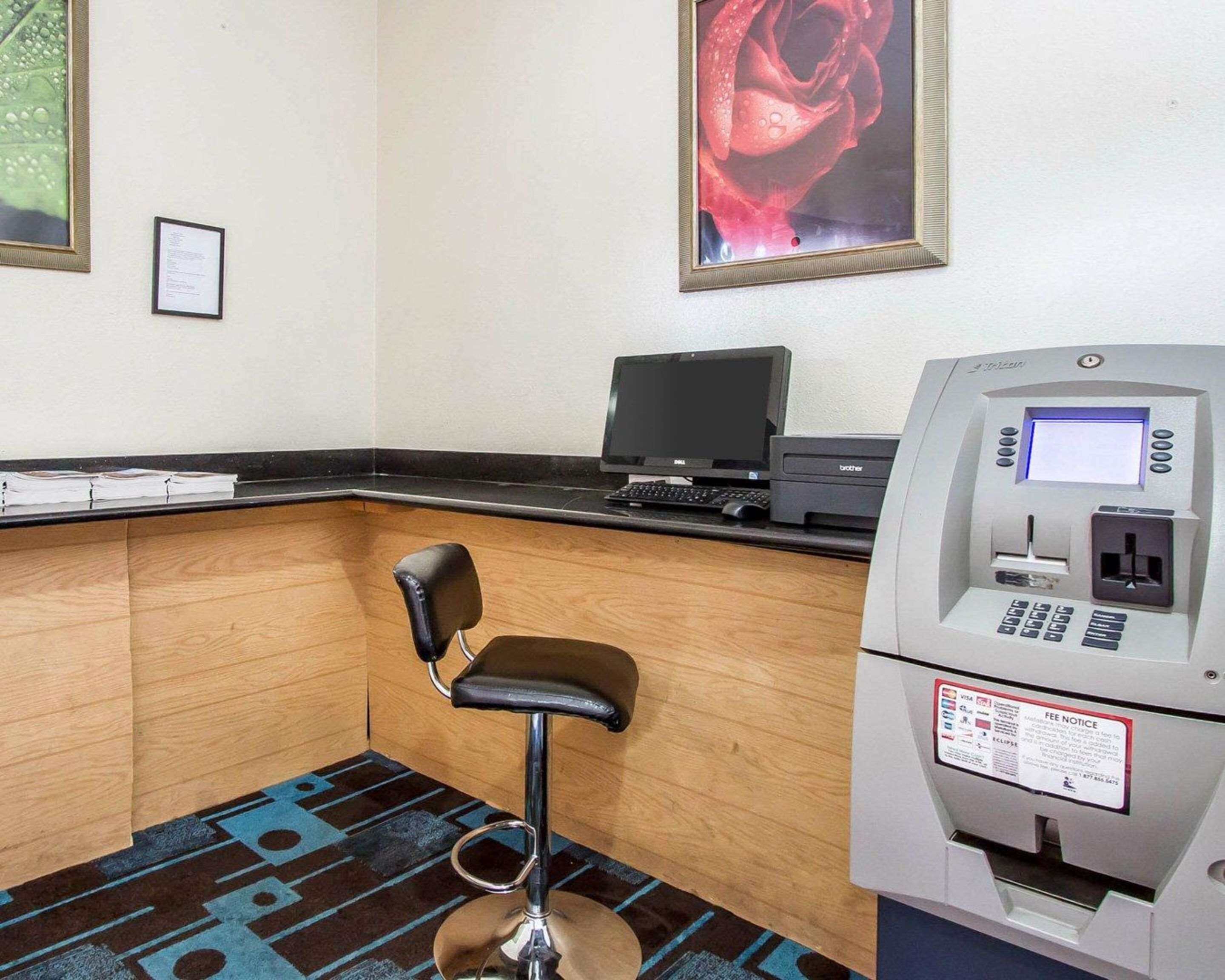 Un petit espace de bureau comprenant un bureau, un ordinateur, une imprimante, une chaise et un terminal de paiement.