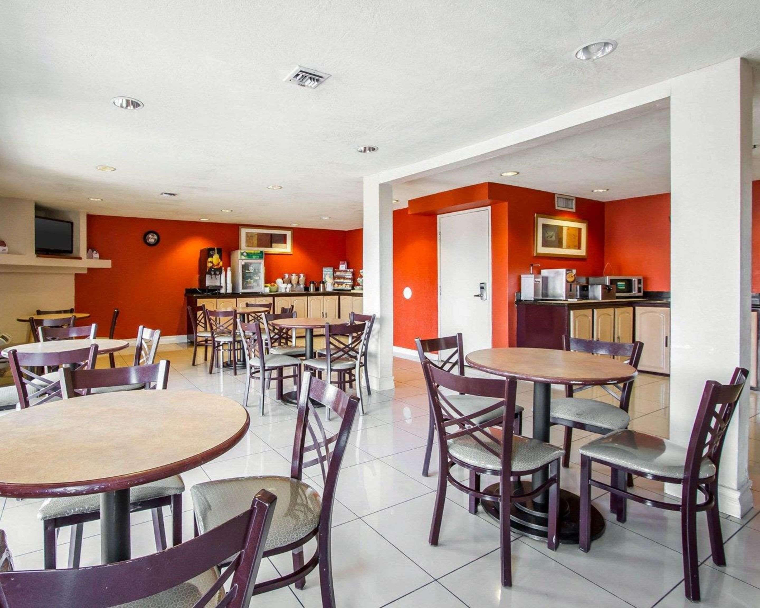 A restaurant with round tables and chairs, a kitchen area, and a television on the wall.