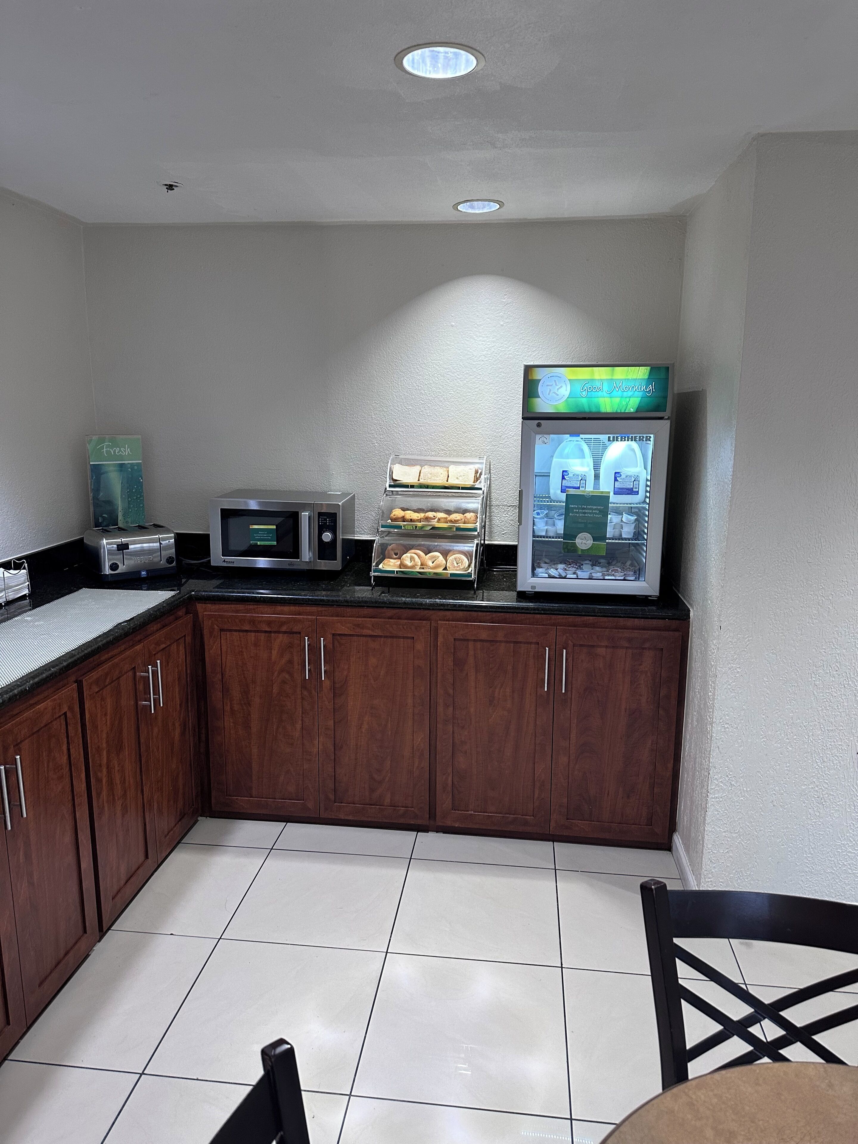 A small kitchenette with a toaster, microwave, and a refrigerator displaying a beverage.