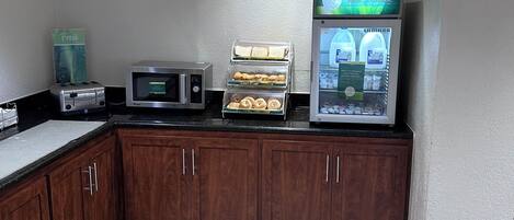 A small kitchenette with a toaster, microwave, and a refrigerator displaying a beverage.