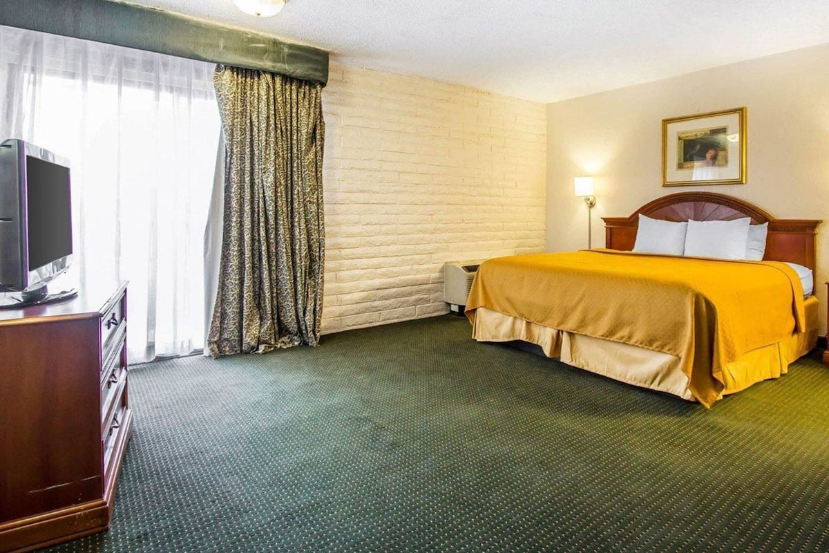 Hotellihuone, jossa on sänky, puinen tv-taso, ikkuna verhoilla ja seinälle ripustettu taulu.