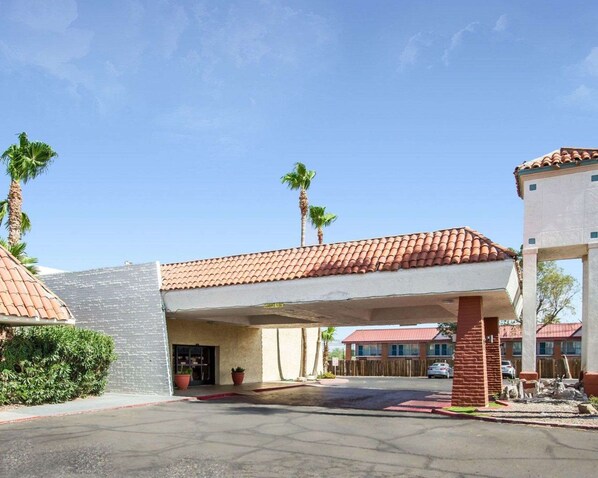A hotel entrance with a covered driveway, palm trees, and a red-tiled roof.