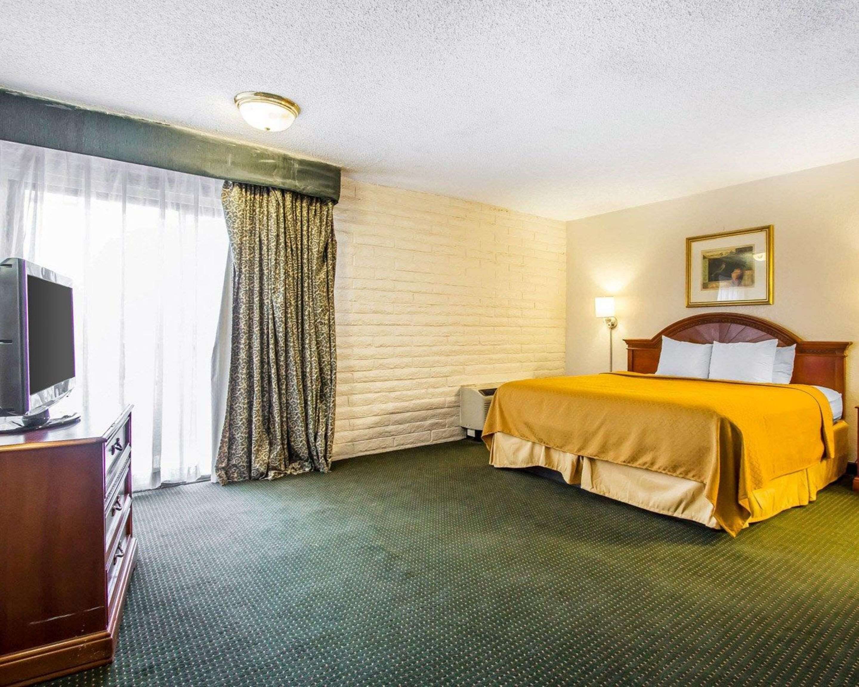 A hotel room with a bed, a television on a wooden cabinet, a window with curtains, and a wall-mounted picture.
