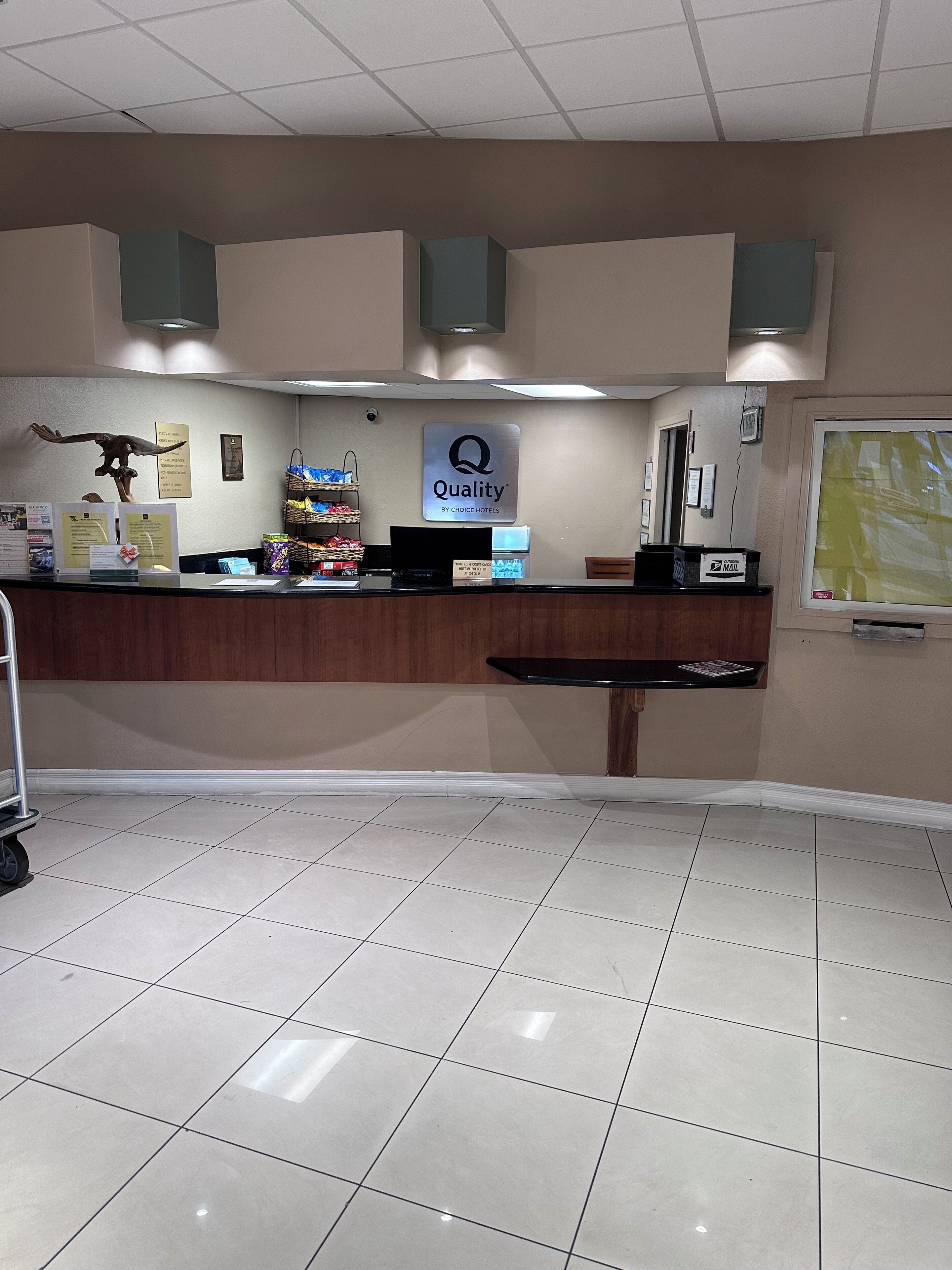 A hotel reception desk with a sign reading "Quality by Choice Hotels," a computer, a mail slot, and a wall-mounted bird sculpture.
