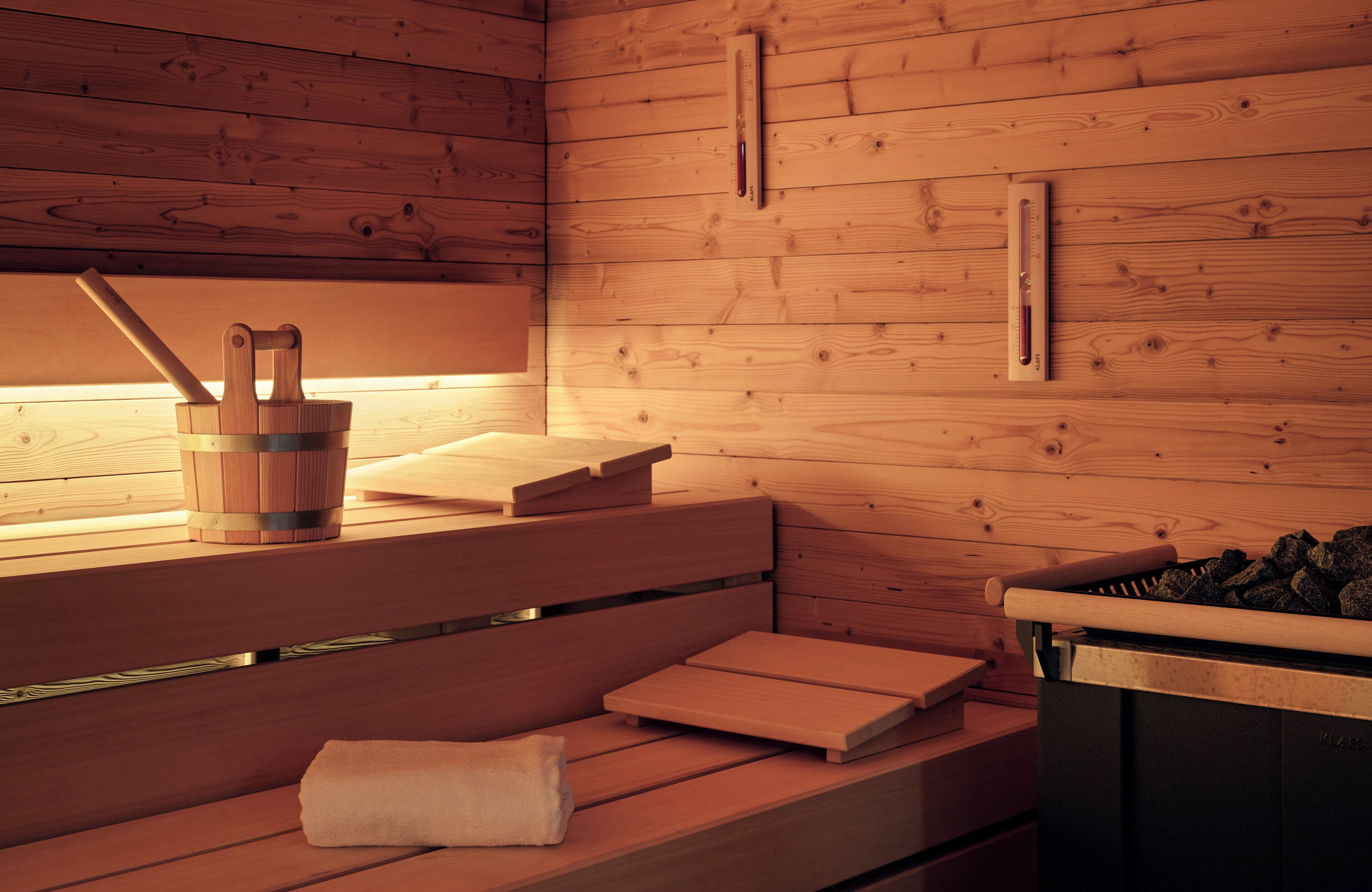 Una sauna de madera con bancos, un cubo y un recipiente con piedras.
