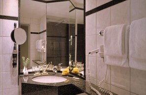 A modern bathroom with a granite countertop, a round mirror, a white sink, and a towel rack.