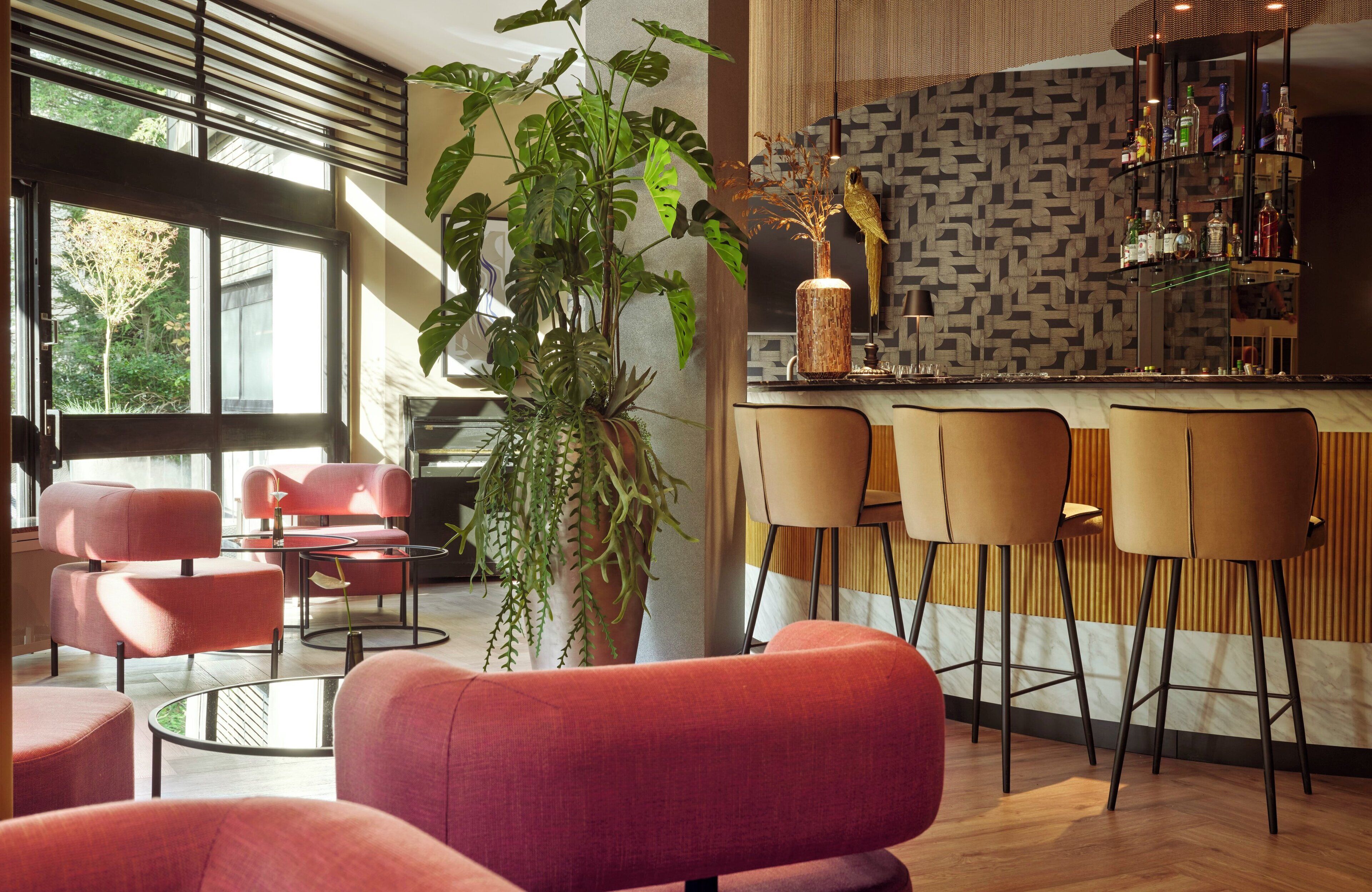 Uma área de bar moderna com parede estampada, uma planta em vaso grande e vários bancos.