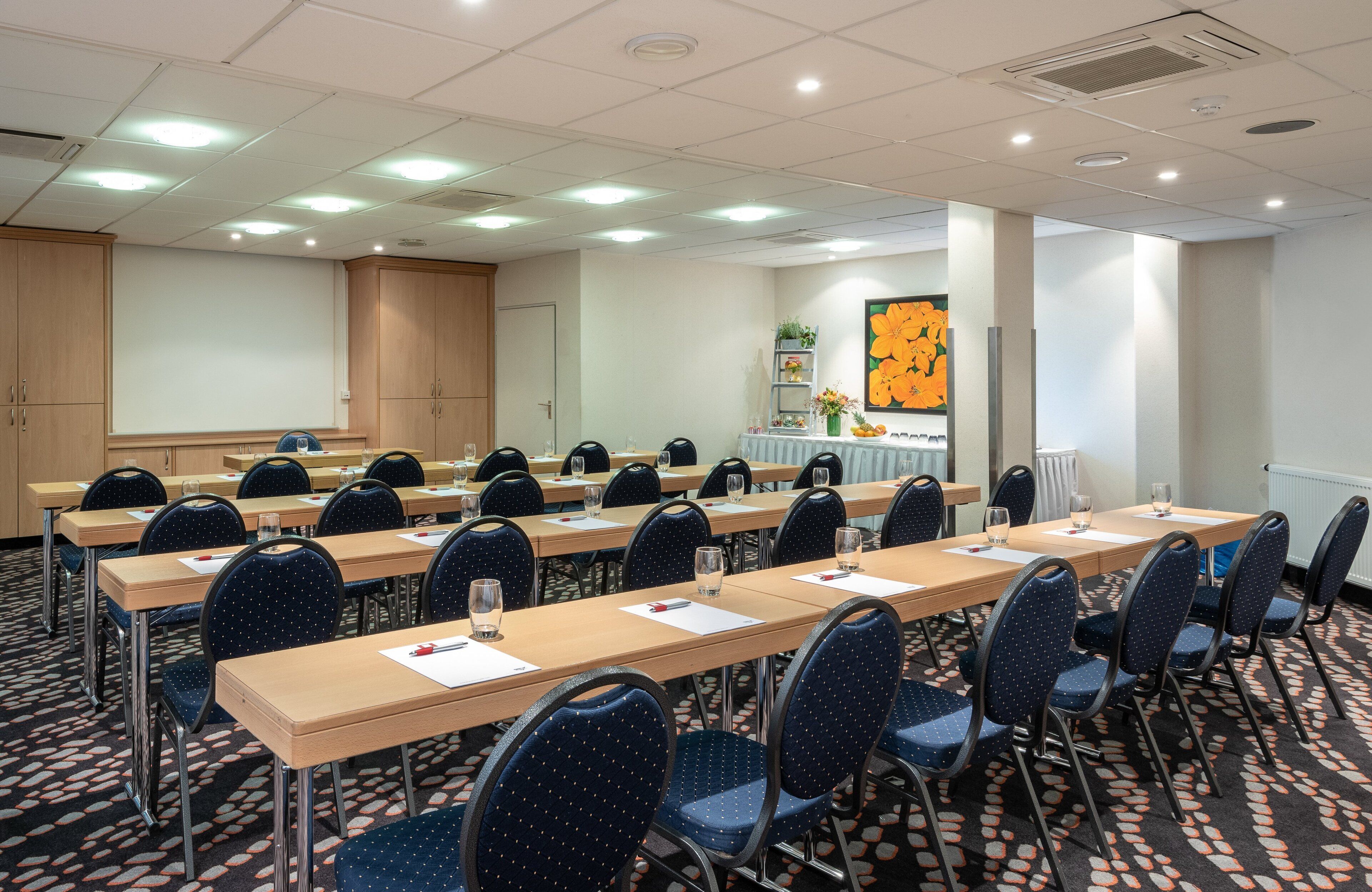 A conference room with long tables, chairs, and a projector screen.