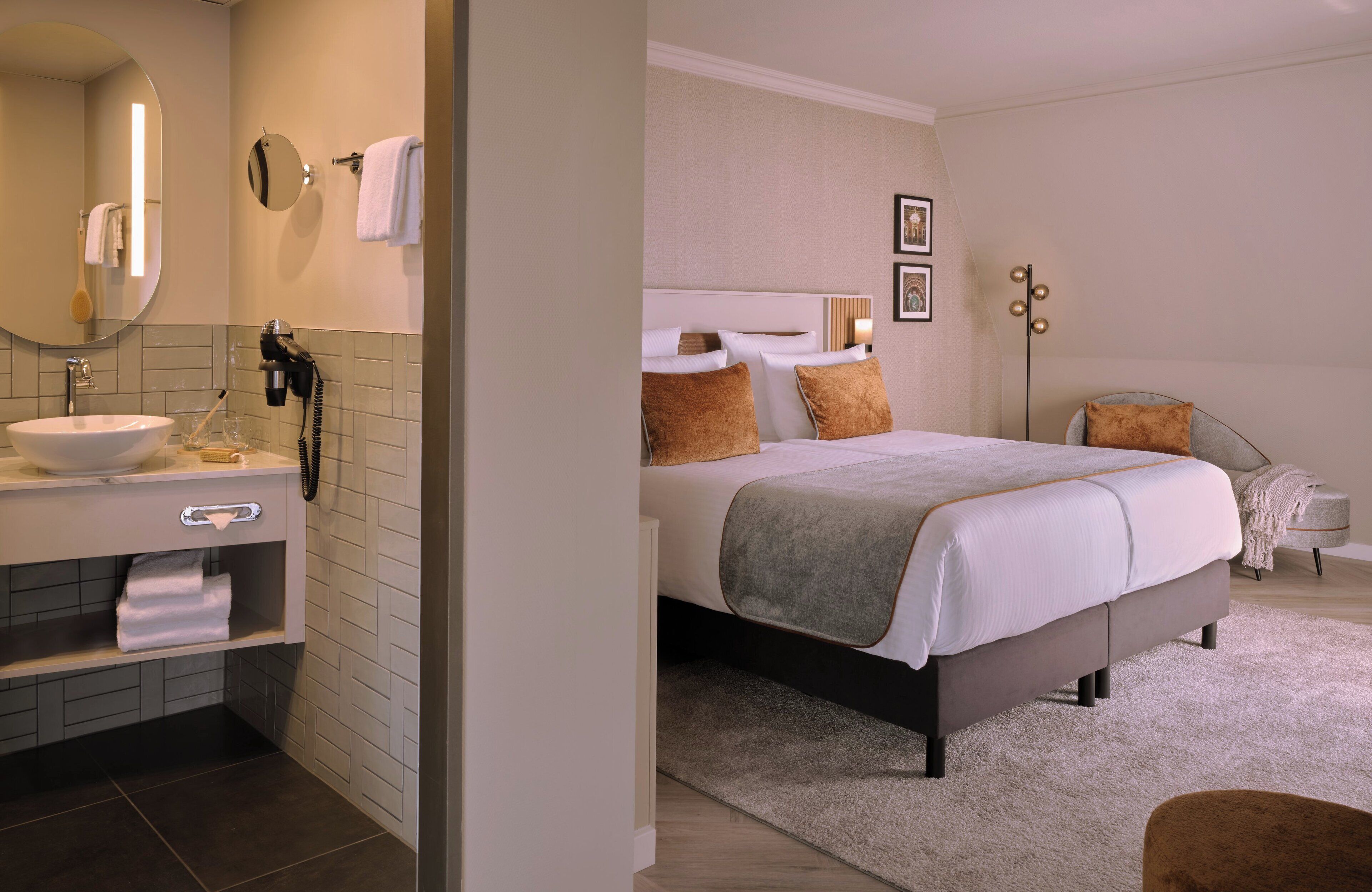 A modern hotel room with a large bed, a bedside table, a mirror, a bathroom with a sink and towel rack.