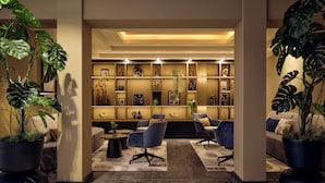 Eine moderne Lobby mit Sitzgelegenheit, einer Wand mit gerahmten Kunstwerken und großen Kübelpflanzen.
