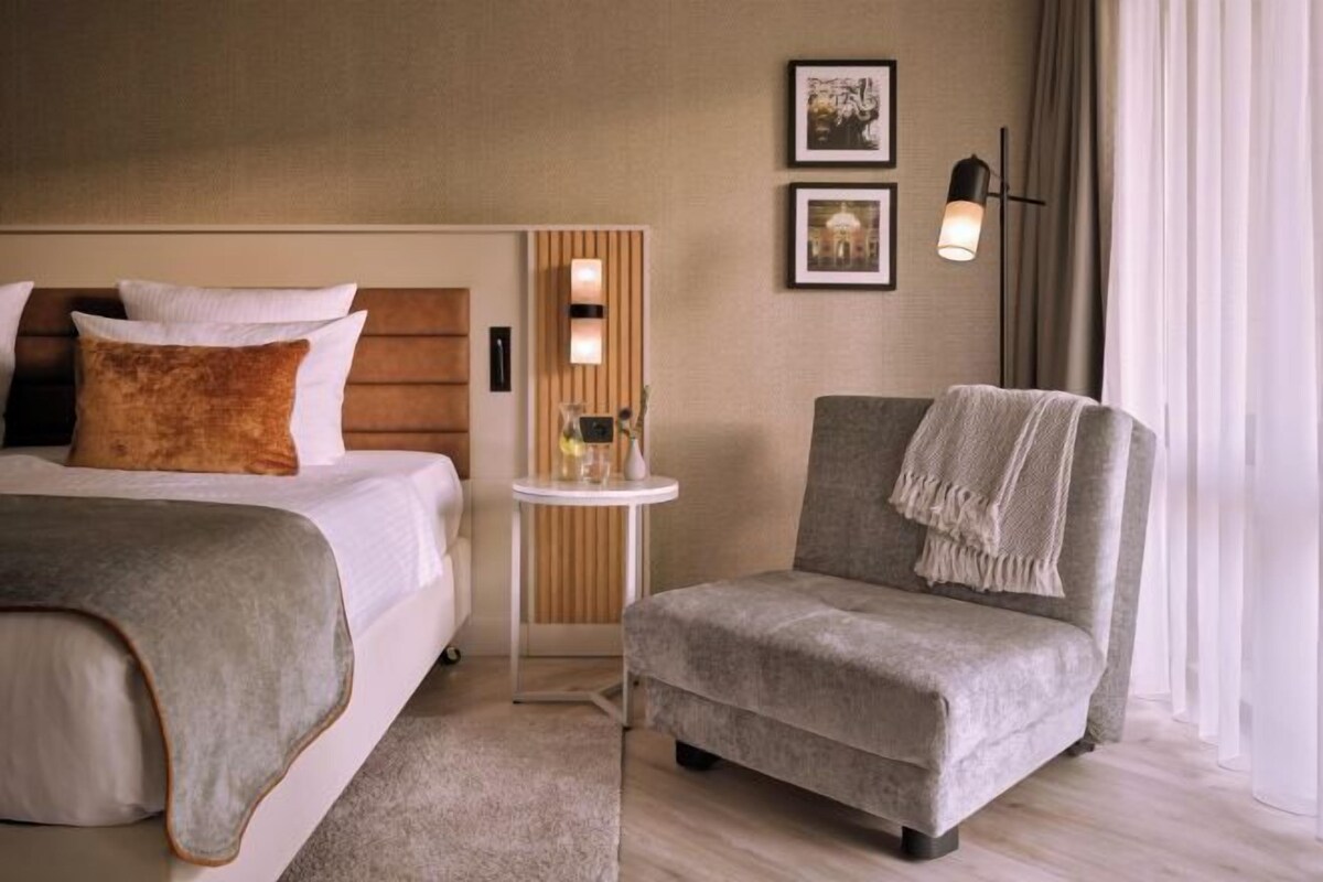 Een hotelkamer met twee bedden, een tafeltje, een stoel en een wandlamp.