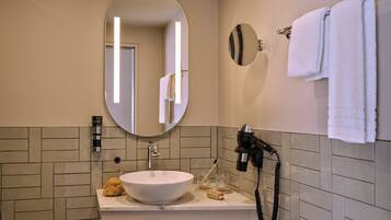 A bathroom with a round mirror, a sink, a towel rack, and a hairdryer.