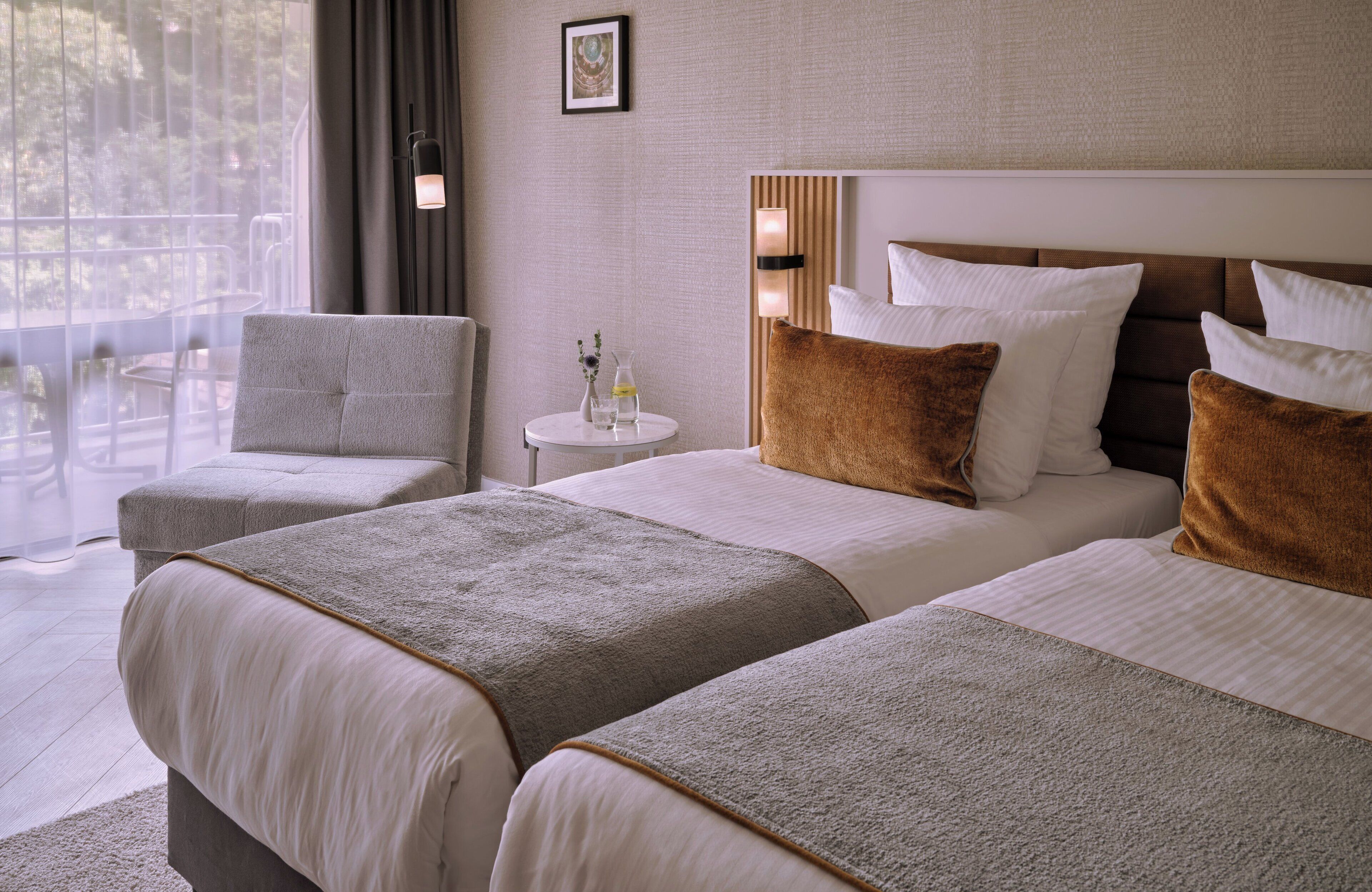 Ein Hotelzimmer mit zwei Betten, einem runden Tisch, einem Stuhl und Blick ins Freie.