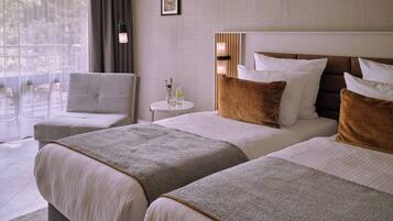 Ein Hotelzimmer mit zwei Betten, einem runden Tisch, einem Stuhl und Blick ins Freie.