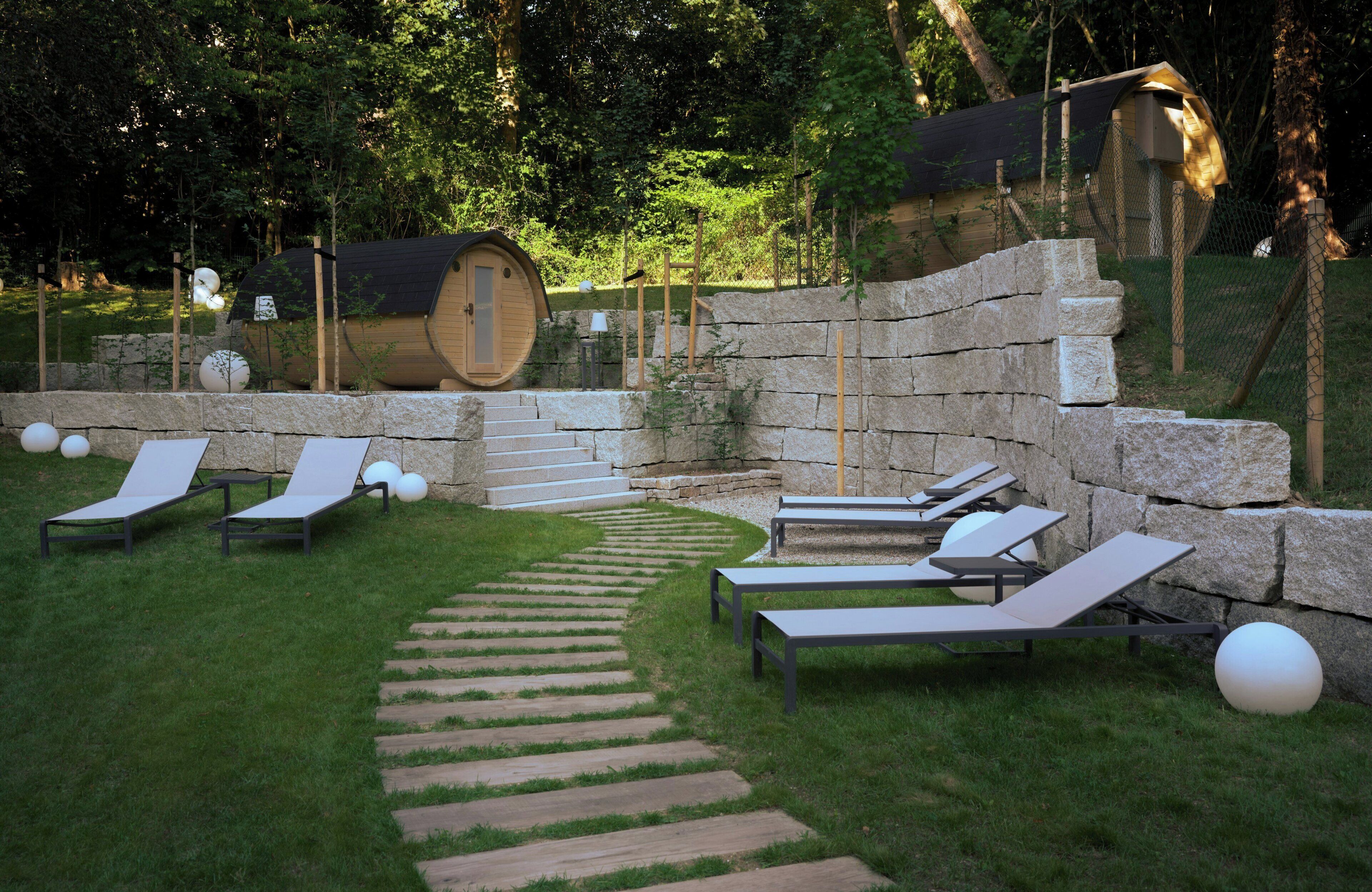 Ein Garten mit Steinmauern, Liegestühlen und einer Holzkonstruktion.
