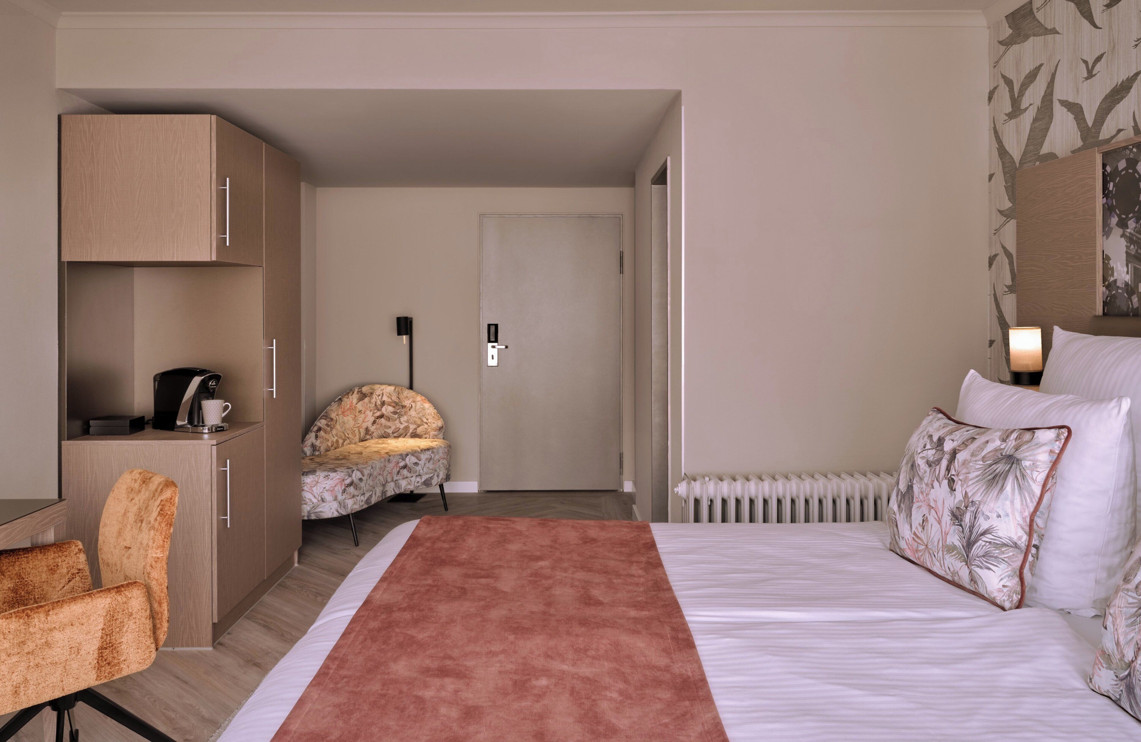 A hotel room with a bed, a desk, a chair, a wardrobe, and a door leading to another room.