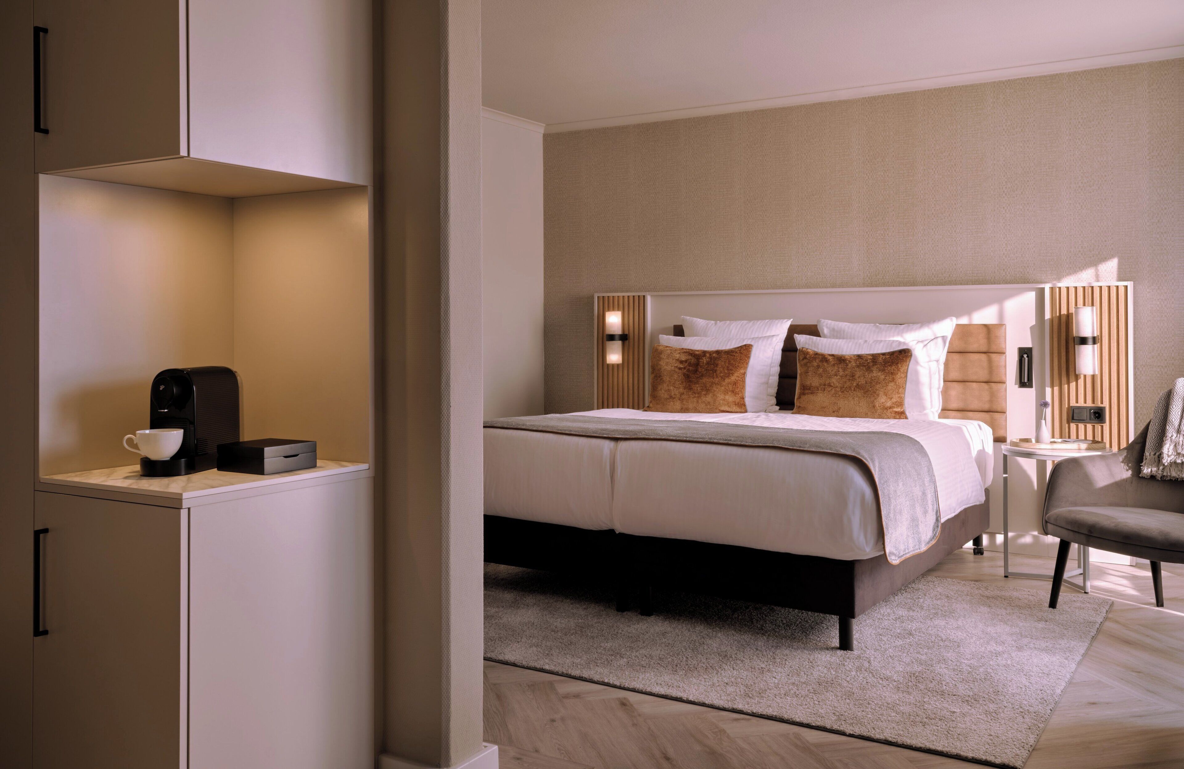 Una habitación de hotel moderna con una cama bien hecha, una cafetera y una mesita auxiliar.