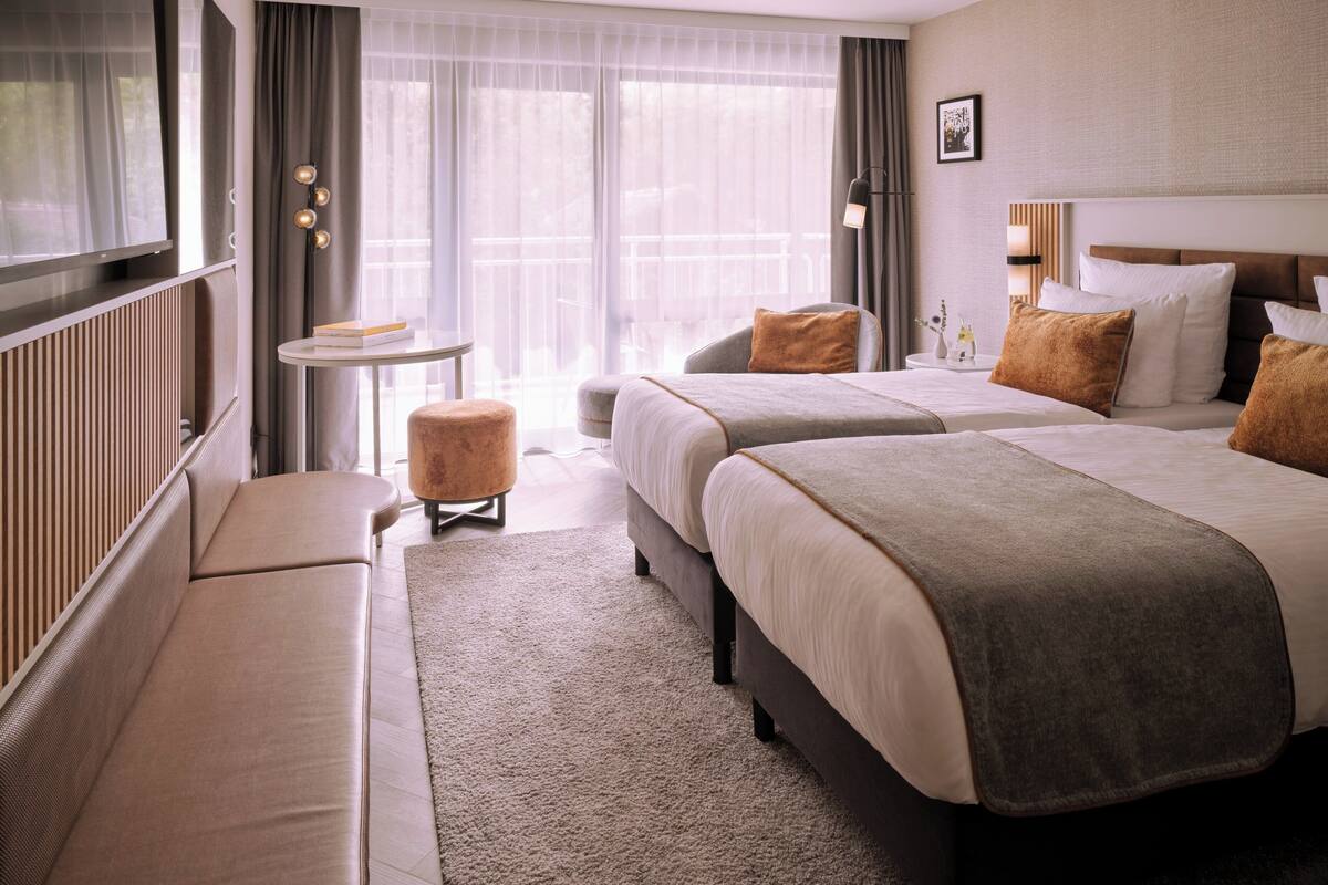 A hotel room with a large bed, a sofa, a small table, and a view of the outdoors.