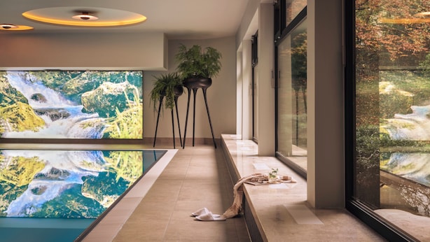Ein modernes Interieur mit einer langen Bank, einem großen Fernsehbildschirm, der einen Wasserfall zeigt, und hohen Stehlampen.