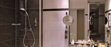 Un baño moderno con ducha envuelta en vidrio, un espejo grande y encimera de granito con lavabo y artículos de aseo.