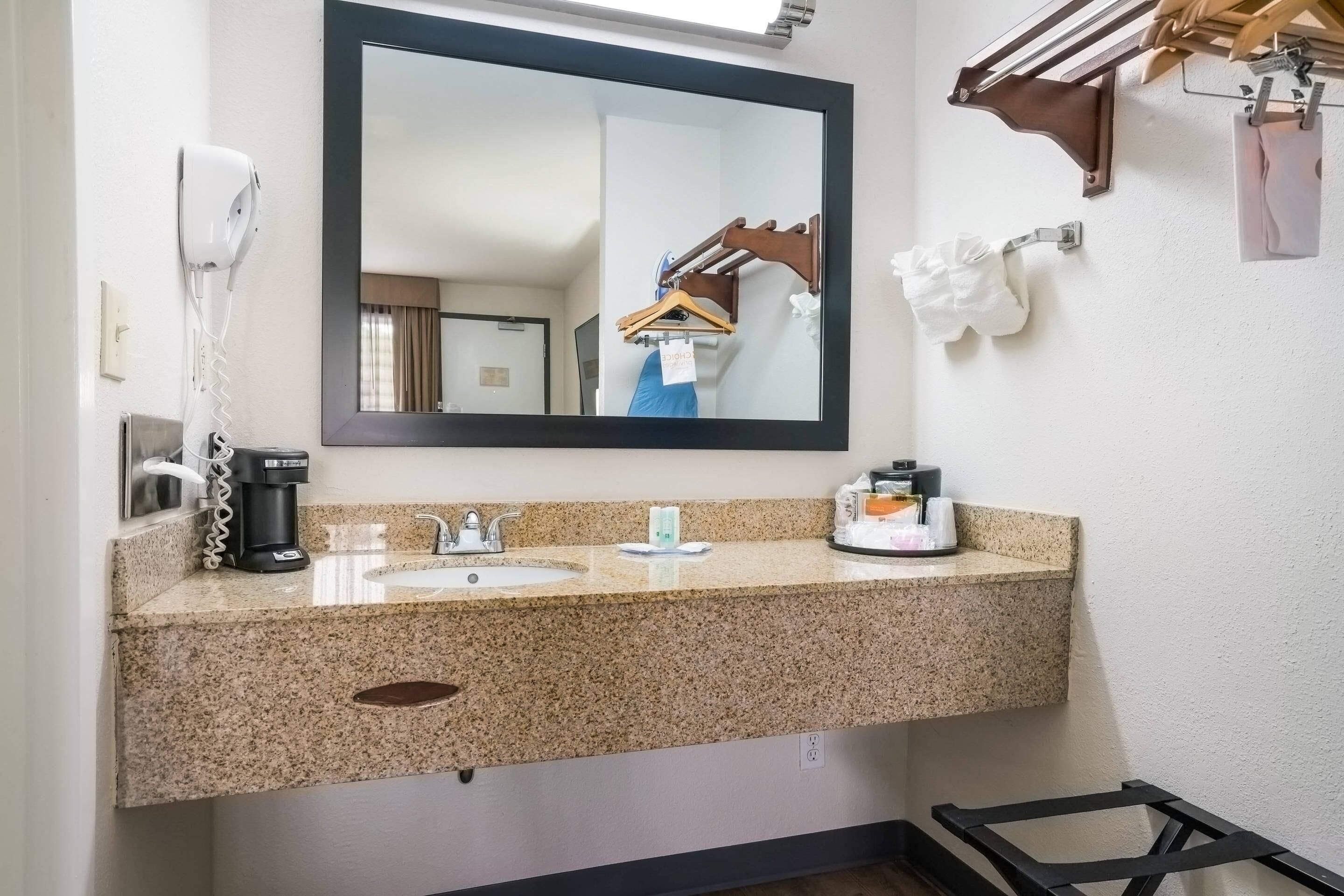 A bathroom with a granite countertop, a sink, a mirror, a hairdryer, and a towel rack.