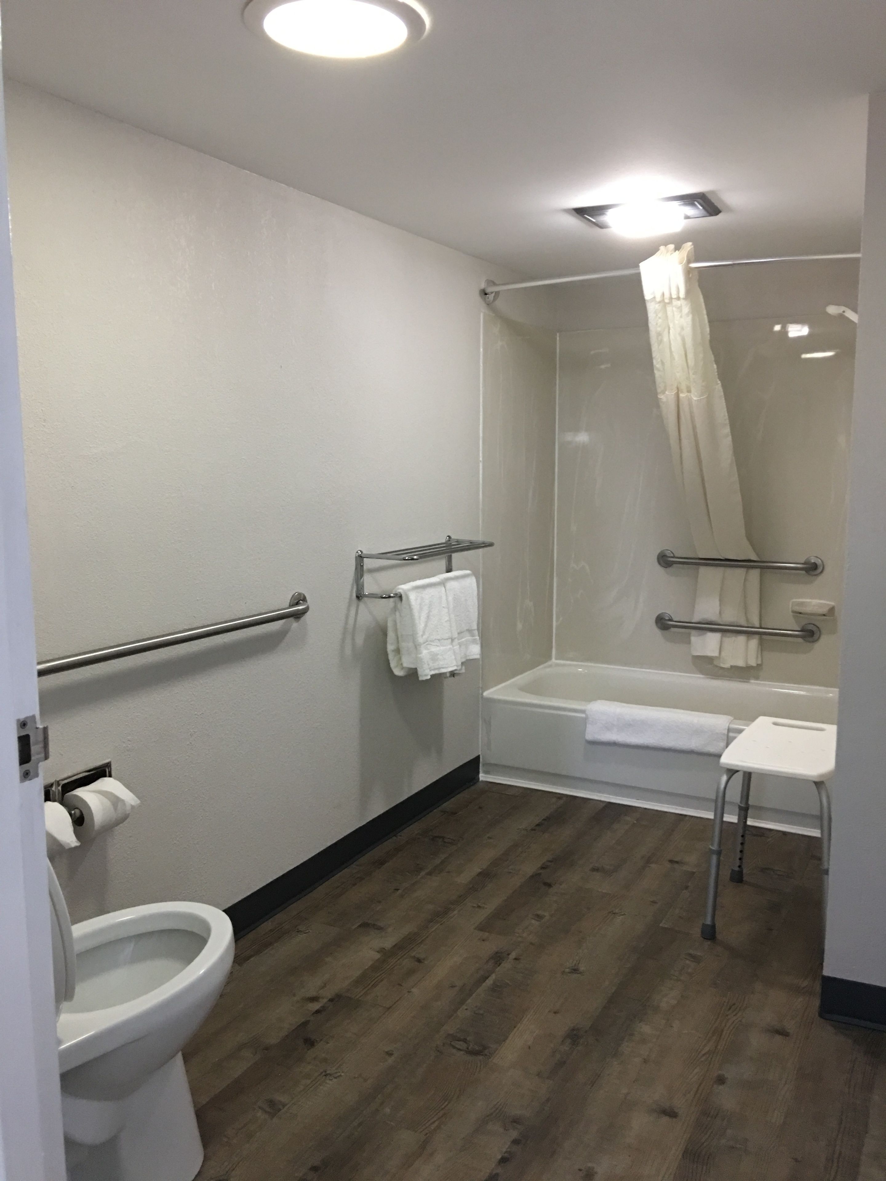A bathroom with a toilet, a shower with a glass door, a bathtub, and a small white stool.