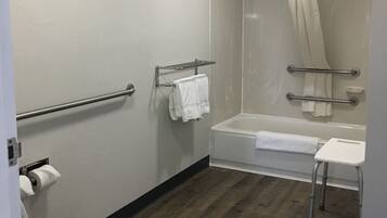 Un baño con inodoro, ducha con puerta de cristal, bañera y un taburete blanco pequeño.