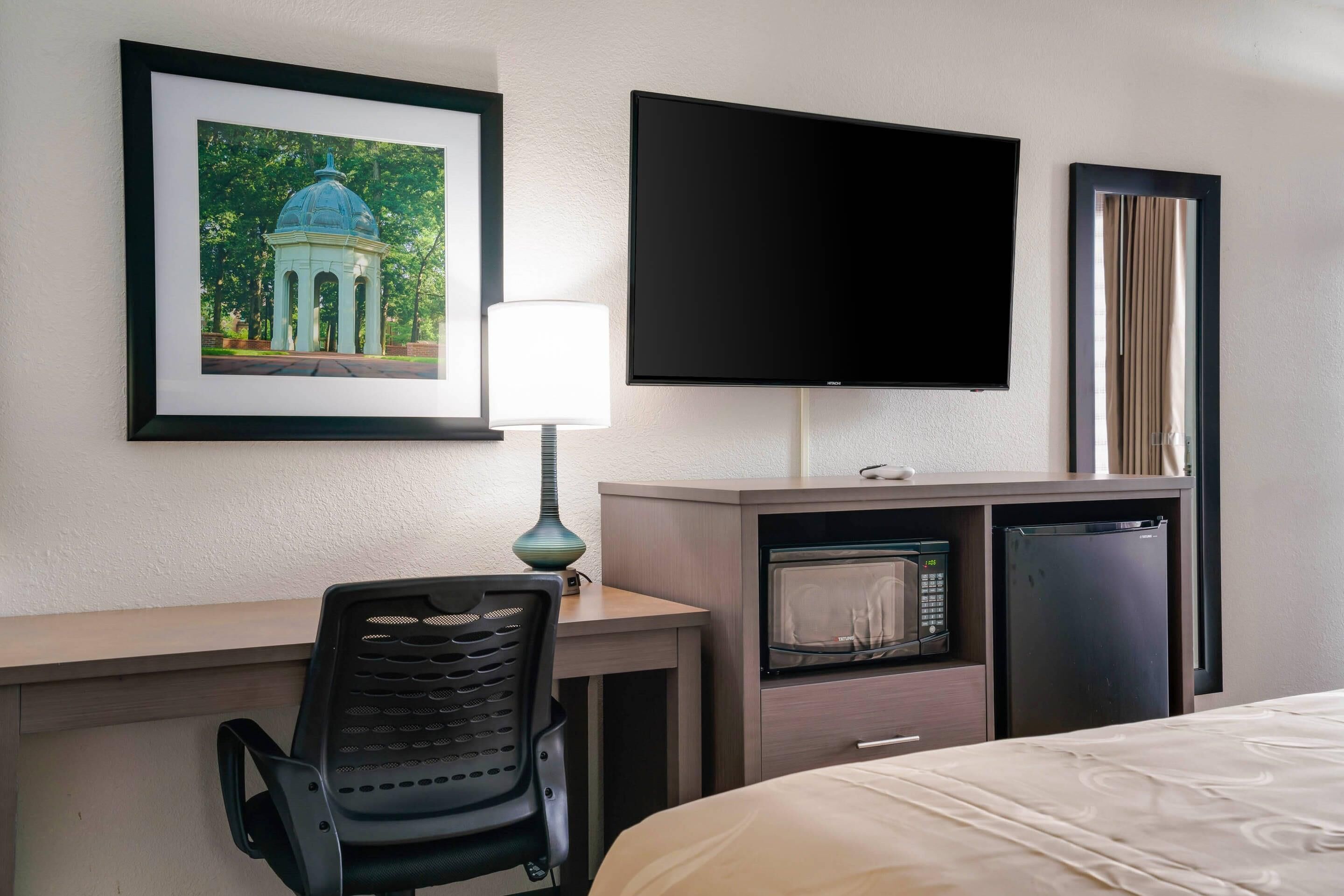 A hotel room with a bed, a desk with a chair, a television, a microwave, and a refrigerator.