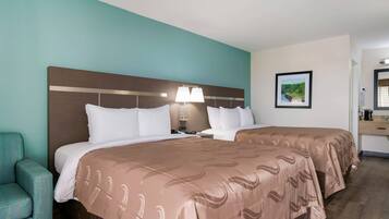 Una habitación de hotel con dos camas, una mesita de noche, una lámpara, un cuadro en la pared y una silla.