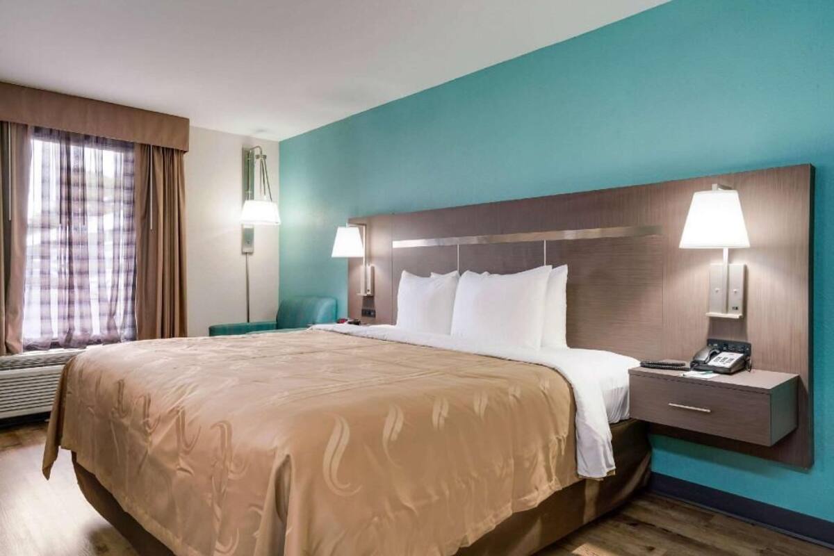 A hotel room with a large bed, two bedside lamps, a nightstand with a phone, and a window with curtains.