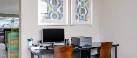 A modern office space with a desk, two chairs, a computer, and a printer. There are framed abstract artworks on the wall.