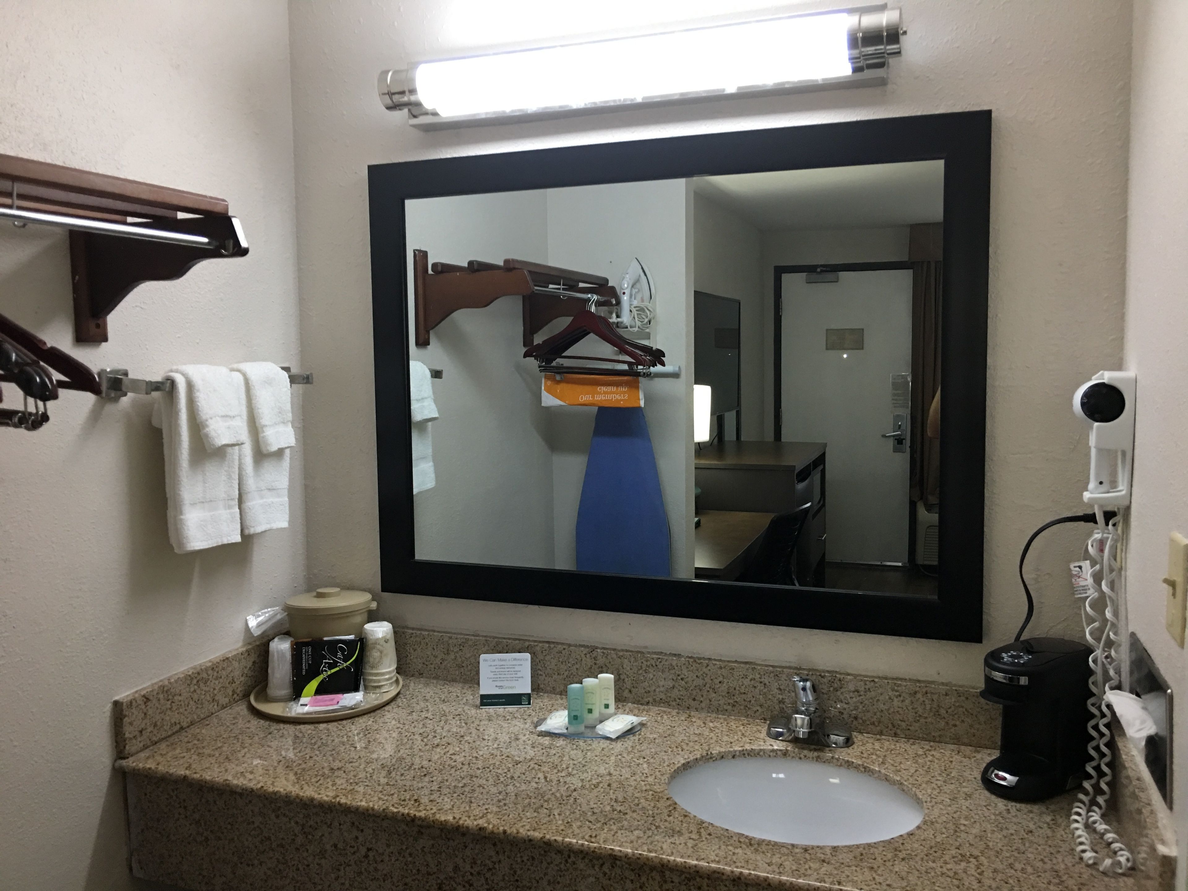 A hotel bathroom with a large mirror, a sink with a countertop, a towel rack, a hairdryer, and a telephone.