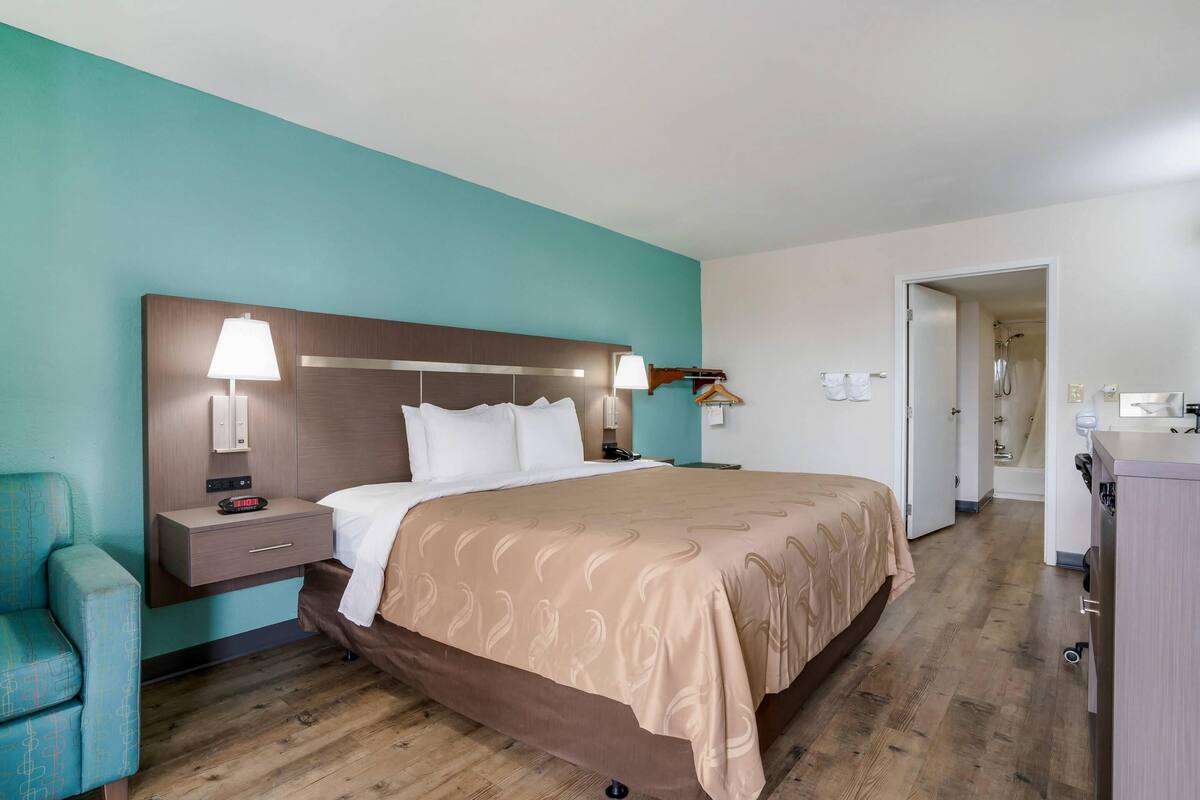 A hotel room with a bed, bedside table, lamp, and a small seating area.