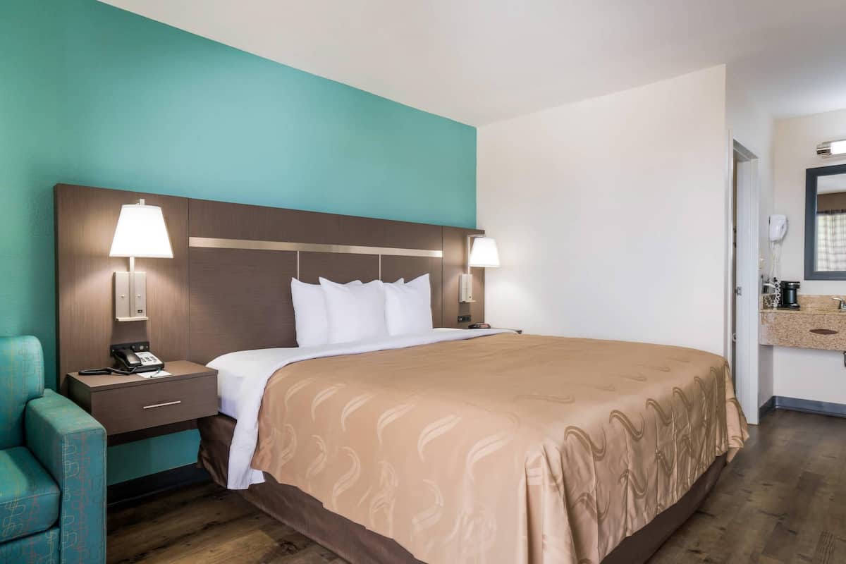 A hotel room with a large bed, two bedside tables with lamps, a small desk, and a chair.